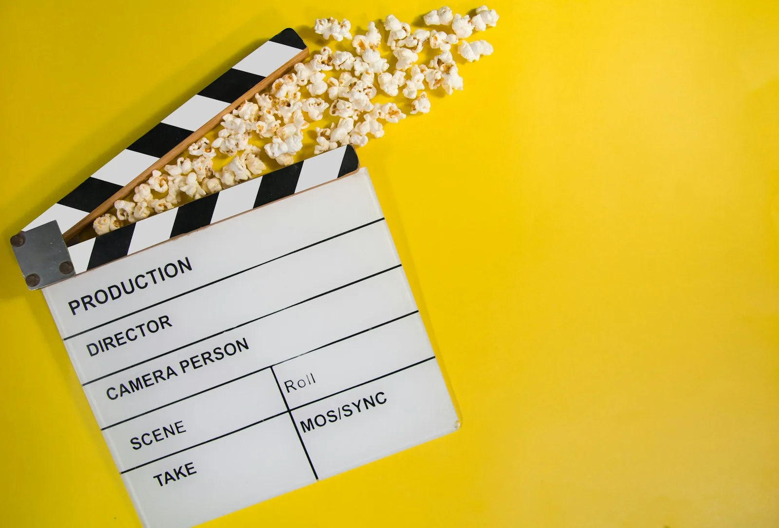 A white film clapperboard and popcorn are arranged on a yellow background.