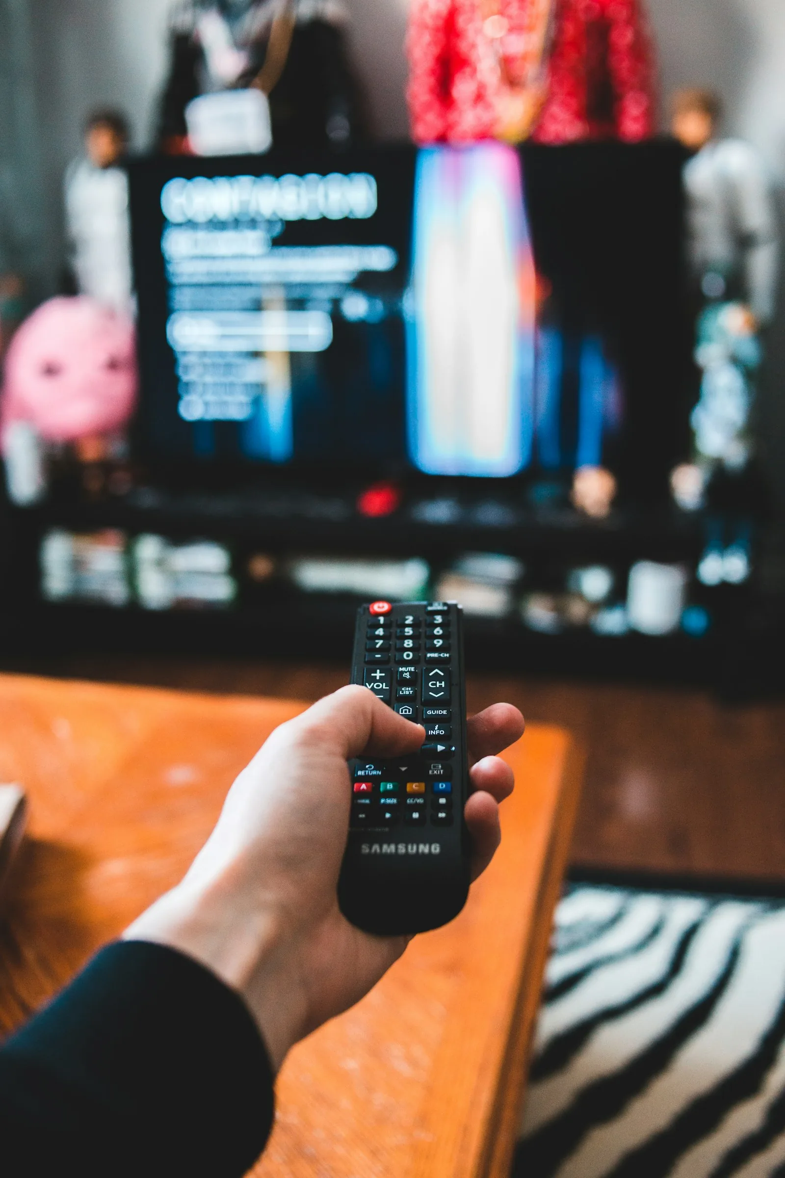 A hand holds a remote control toward a television with an out-of-focus streaming interface.