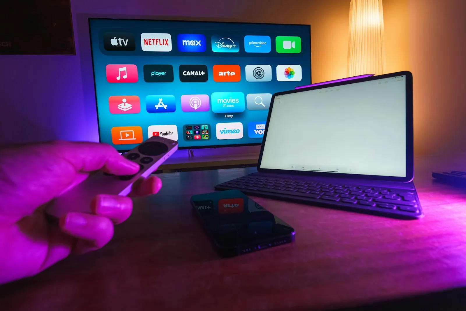 A television shows streaming-service apps beside a tablet, phone and remote control.
